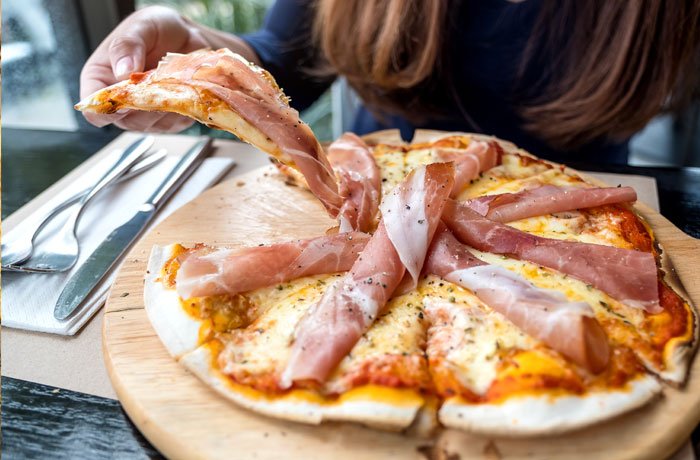 Jakie wino do pizzy z szynką - kobieta jedząca pizzę z Prosciutto di Parma